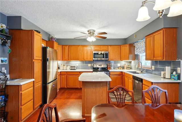 kitchen with light countertops, a sink, a center island, appliances with stainless steel finishes, and ceiling fan
