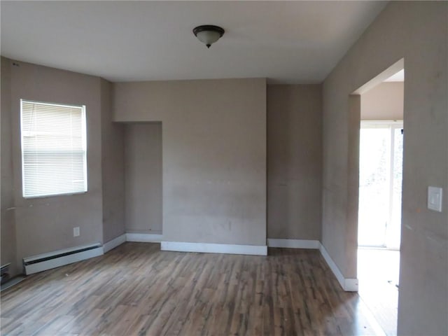 spare room with a healthy amount of sunlight, baseboards, baseboard heating, and wood finished floors