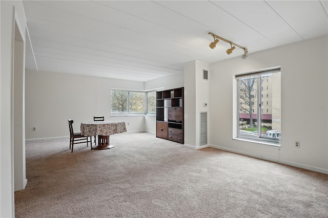 unfurnished living room with track lighting, visible vents, carpet flooring, and baseboards