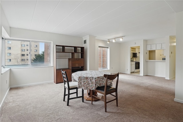 dining space featuring light colored carpet, baseboards, and track lighting