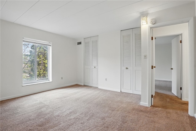 unfurnished bedroom featuring visible vents, baseboards, multiple closets, and carpet flooring