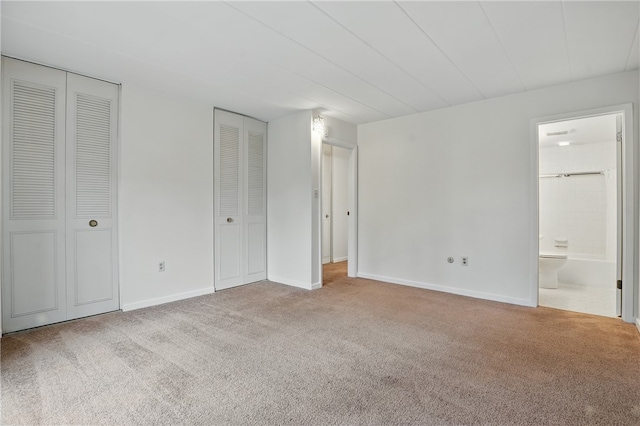 unfurnished bedroom featuring ensuite bath, carpet, multiple closets, and baseboards
