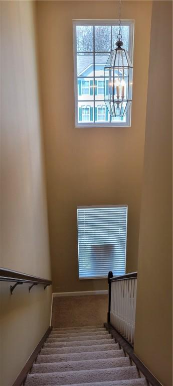 stairway with baseboards, an inviting chandelier, and carpet