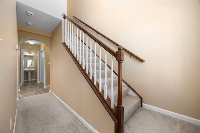 staircase featuring baseboards, arched walkways, and carpet