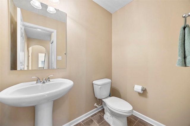half bath with toilet, tile patterned flooring, a sink, and baseboards