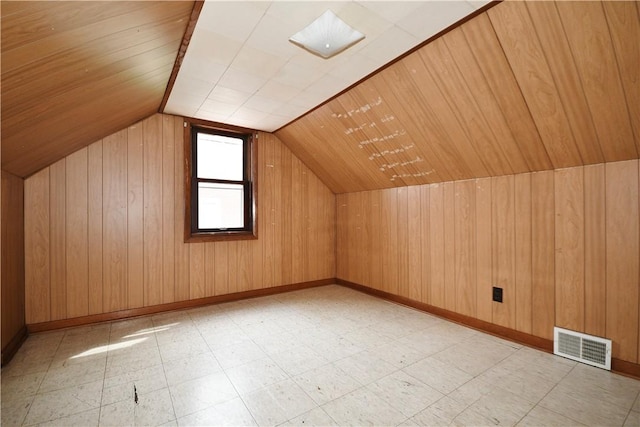 additional living space with light floors, vaulted ceiling, wood walls, and visible vents