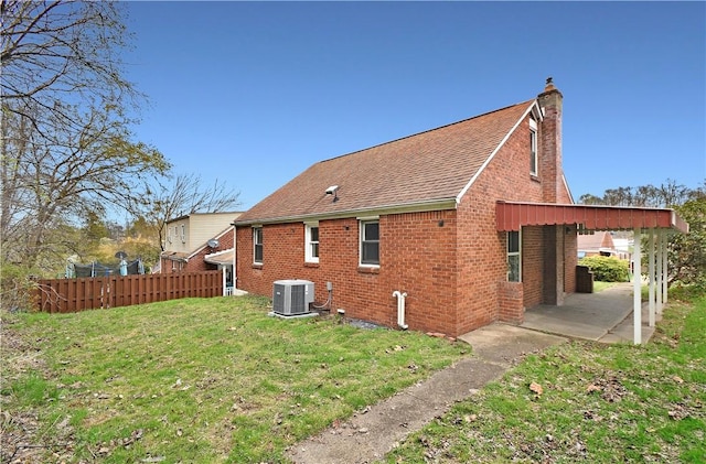 rear view of house with a lawn, a chimney, fence, cooling unit, and brick siding