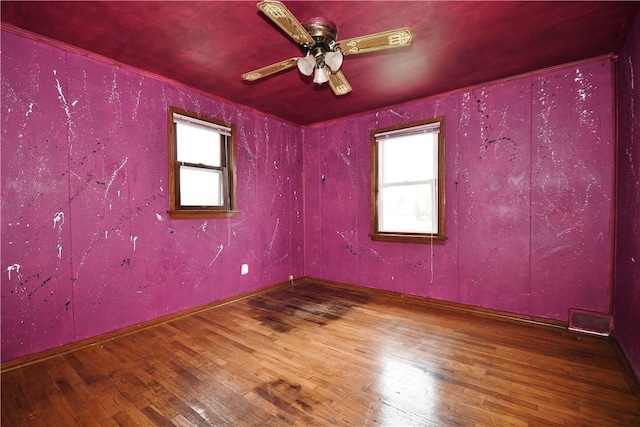spare room featuring hardwood / wood-style flooring, ceiling fan, visible vents, and plenty of natural light