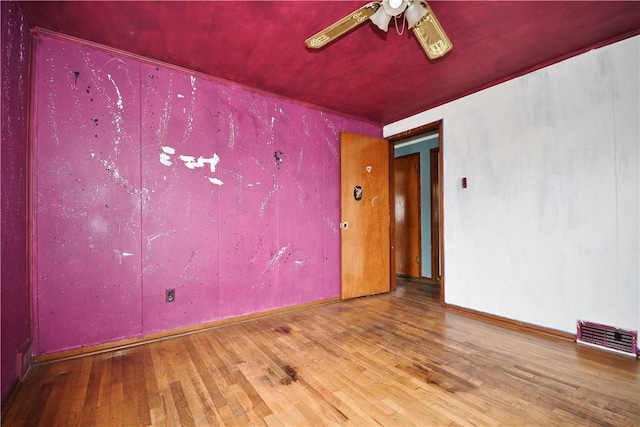 unfurnished room with wood finished floors, visible vents, a ceiling fan, and baseboards