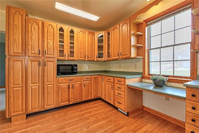 kitchen featuring black microwave, glass insert cabinets, tasteful backsplash, and light wood-style flooring