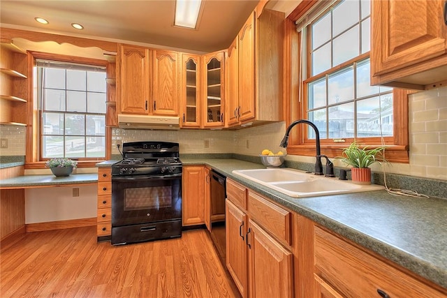 kitchen featuring glass insert cabinets, under cabinet range hood, a sink, light wood finished floors, and black appliances