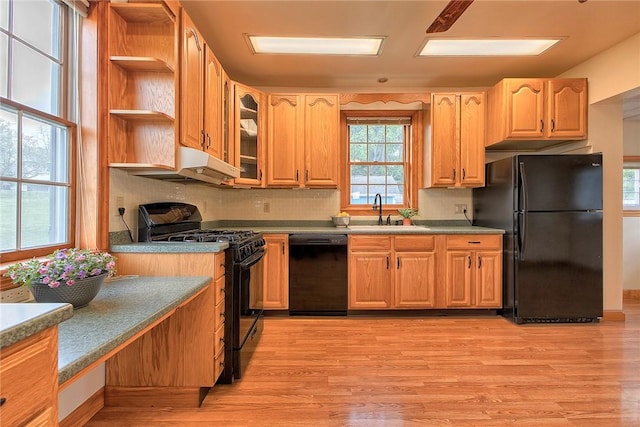 kitchen featuring a sink, light wood-style floors, decorative backsplash, under cabinet range hood, and black appliances
