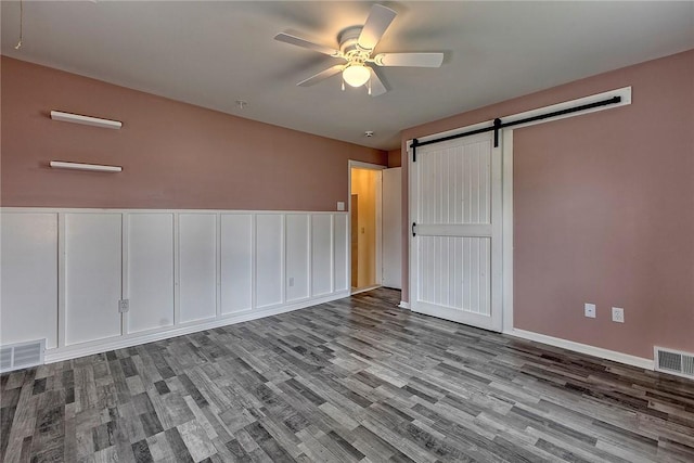 spare room with a ceiling fan, visible vents, a barn door, and wood finished floors