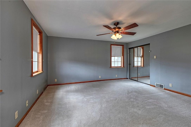 carpeted empty room with ceiling fan, visible vents, plenty of natural light, and baseboards