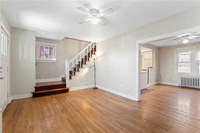 unfurnished living room featuring ceiling fan, light wood finished floors, stairs, and radiator