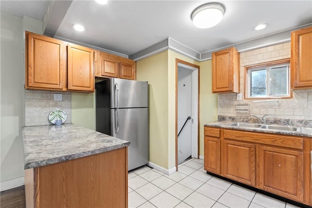 kitchen featuring baseboards, a sink, backsplash, and freestanding refrigerator