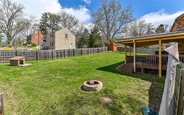 view of yard with a storage unit, a fenced backyard, a fire pit, a wooden deck, and an outdoor structure