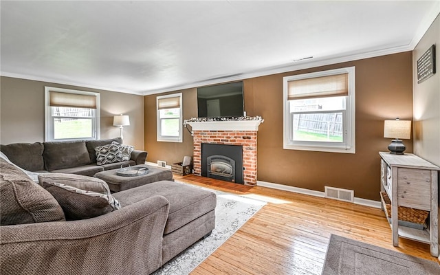 living room with a brick fireplace, visible vents, ornamental molding, and wood-type flooring