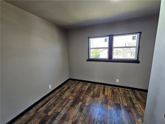 spare room with baseboards and dark wood-style flooring