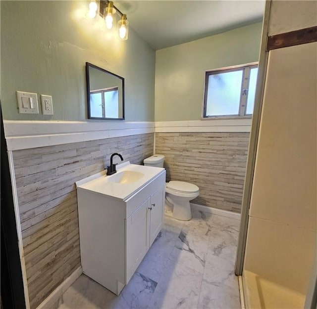 bathroom with tile walls, vanity, toilet, a wainscoted wall, and marble finish floor
