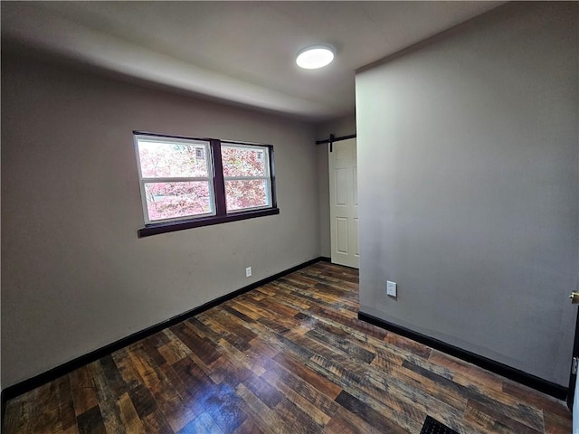 unfurnished room with baseboards, a barn door, and dark wood finished floors