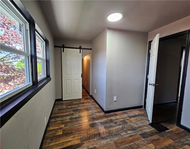 unfurnished bedroom with a barn door, dark wood finished floors, and baseboards