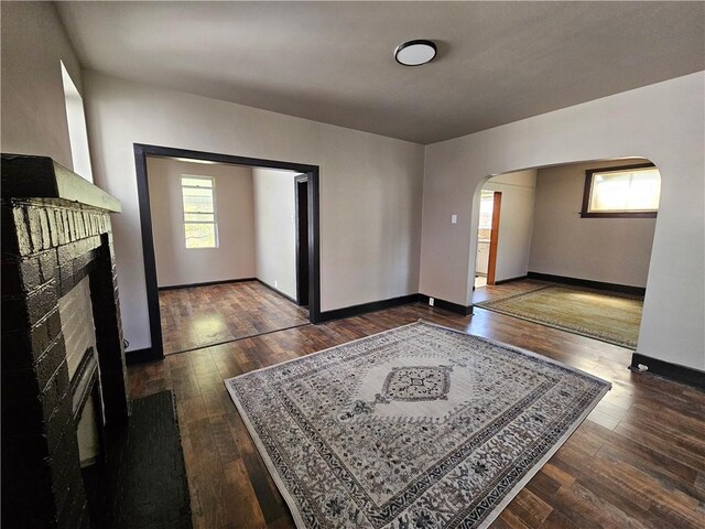 living room with a fireplace, dark wood-type flooring, baseboards, and arched walkways