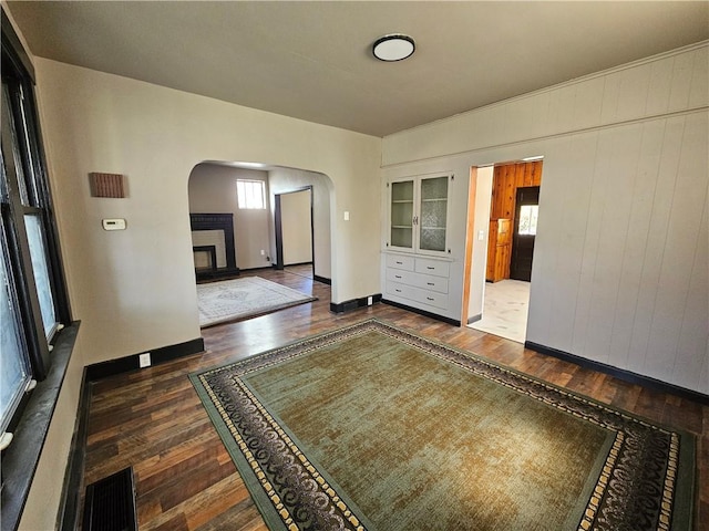 spare room featuring hardwood / wood-style floors, baseboards, arched walkways, and plenty of natural light