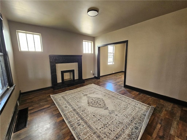 unfurnished living room with baseboards, visible vents, a fireplace, and dark wood-type flooring