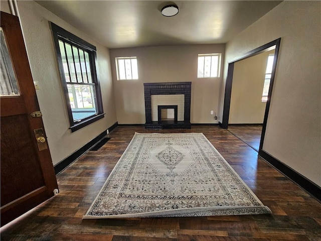 unfurnished living room with a fireplace, dark wood finished floors, baseboards, and plenty of natural light