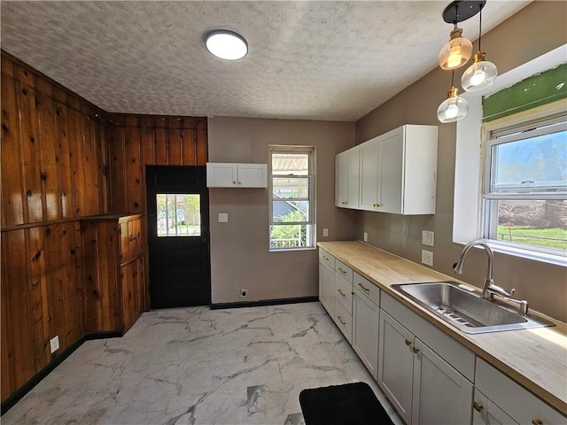 kitchen with a sink, a healthy amount of sunlight, marble finish floor, white cabinetry, and a textured ceiling