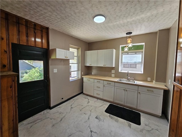 kitchen with a textured ceiling, a sink, light countertops, marble finish floor, and hanging light fixtures