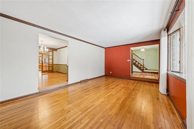 unfurnished living room with an inviting chandelier, visible vents, ornamental molding, hardwood / wood-style flooring, and stairs