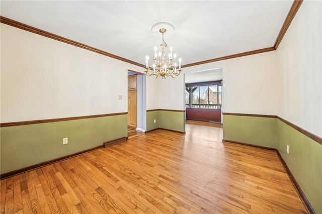 spare room featuring an inviting chandelier, ornamental molding, light wood-style floors, and baseboards