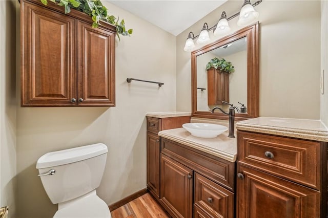 bathroom with toilet, vanity, wood finished floors, and baseboards