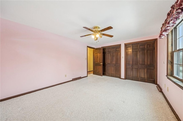 unfurnished bedroom featuring two closets, ceiling fan, baseboards, and light colored carpet