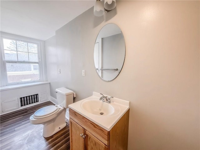 bathroom featuring toilet, visible vents, baseboards, wood finished floors, and vanity