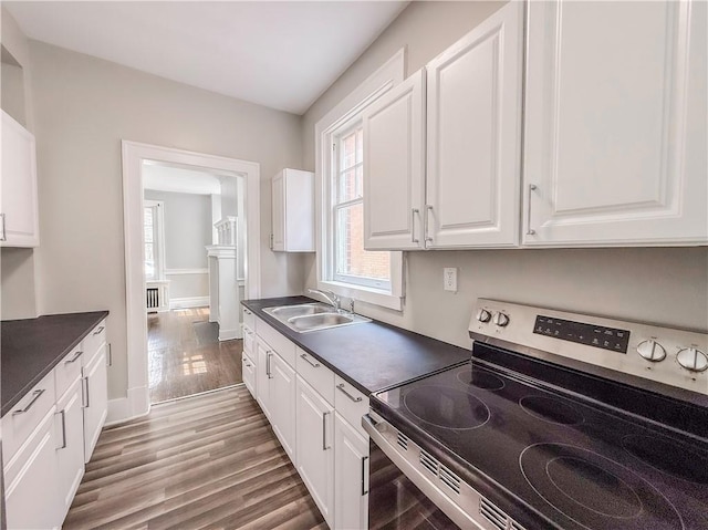 kitchen with white cabinets, light wood-style flooring, a sink, dark countertops, and stainless steel range with electric stovetop