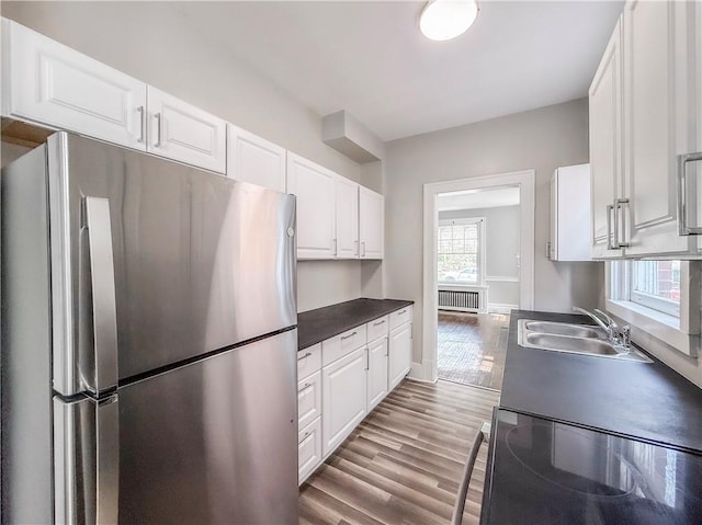 kitchen featuring a sink, dark countertops, freestanding refrigerator, white cabinetry, and black electric range