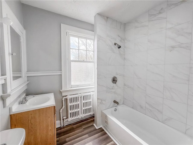 bathroom with a textured ceiling,  shower combination, radiator, wood finished floors, and vanity