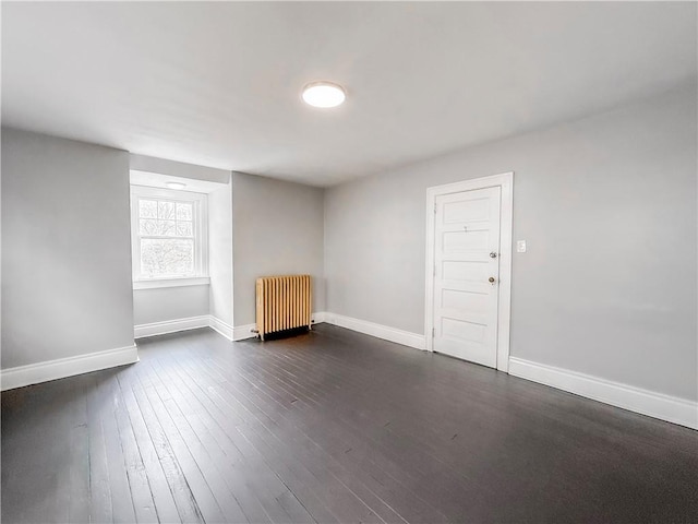 empty room with dark wood finished floors, radiator, and baseboards