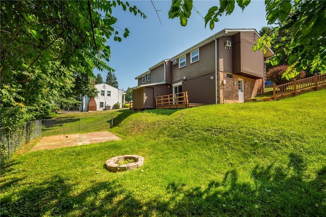 rear view of house featuring a fire pit, brick siding, fence, and a lawn