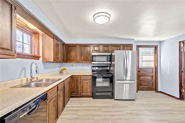 kitchen with light wood-style flooring, light countertops, a sink, and black appliances