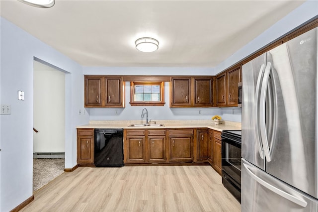 kitchen featuring light countertops, a sink, light wood-style floors, black appliances, and baseboard heating