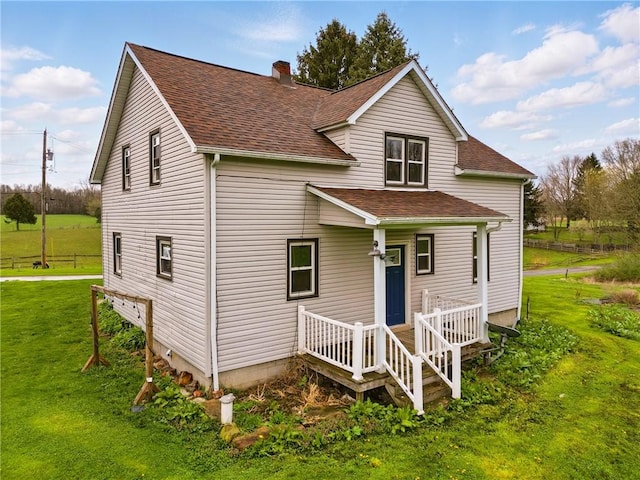 view of front of property with covered porch, a chimney, a shingled roof, and a front lawn