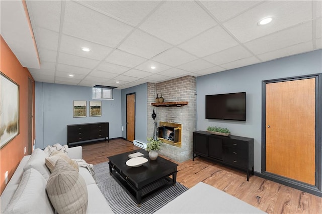 2925 Mcneal Rd, Hampton, PA 15101 - living room featuring a baseboard heating unit, wood finished floors, a brick fireplace, and a paneled ceiling