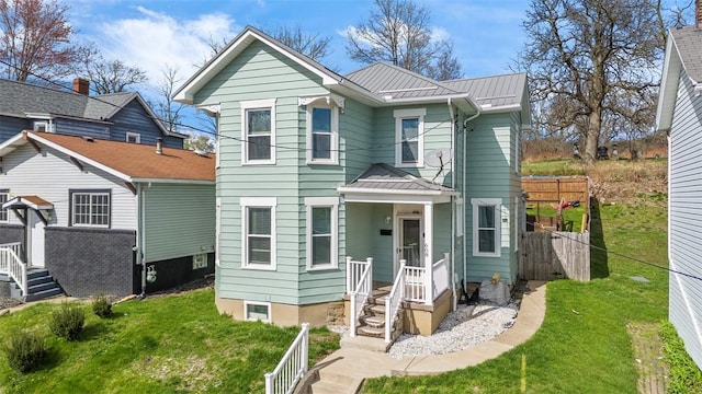 victorian house featuring a standing seam roof, fence, a front yard, and metal roof