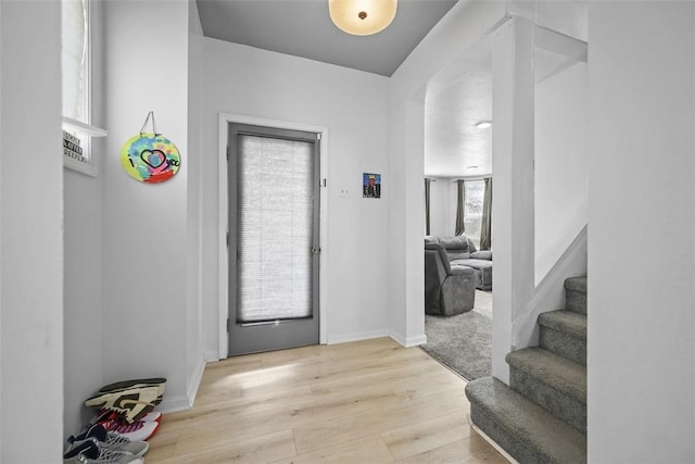 foyer with light wood-type flooring, baseboards, and stairway