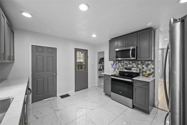 kitchen featuring light stone countertops, backsplash, appliances with stainless steel finishes, and gray cabinets