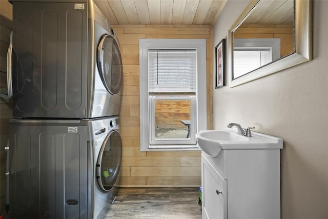 laundry room with wood finished floors, a sink, wooden walls, stacked washer and dryer, and laundry area